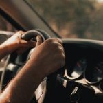 Mãos de um motorista segurando o volante dentro de um carro.