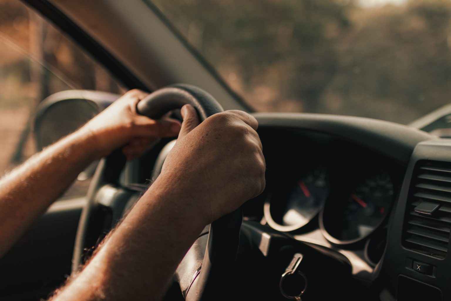 Mãos de um motorista segurando o volante dentro de um carro.