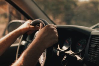 Mãos de um motorista segurando o volante dentro de um carro.