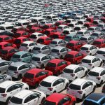 Vista aérea de carros novos de diferentes cores estacionados em fileiras em um grande pátio.