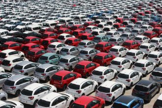 Vista aérea de carros novos de diferentes cores estacionados em fileiras em um grande pátio.