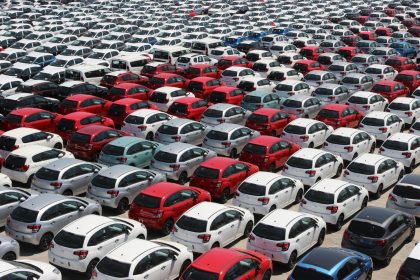 Vista aérea de carros novos de diferentes cores estacionados em fileiras em um grande pátio.