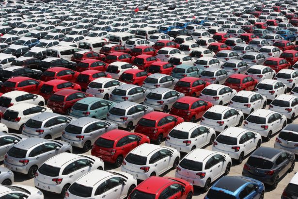 Vista aérea de carros novos de diferentes cores estacionados em fileiras em um grande pátio.