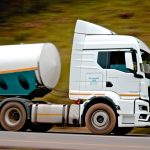 Caminhão-tanque branco em movimento em uma rodovia, com efeito de velocidade.