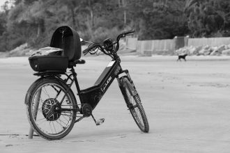 Bicicleta elétrica apoiada na areia da praia de Guaratuba, no Paraná, em imagem em preto e branco.