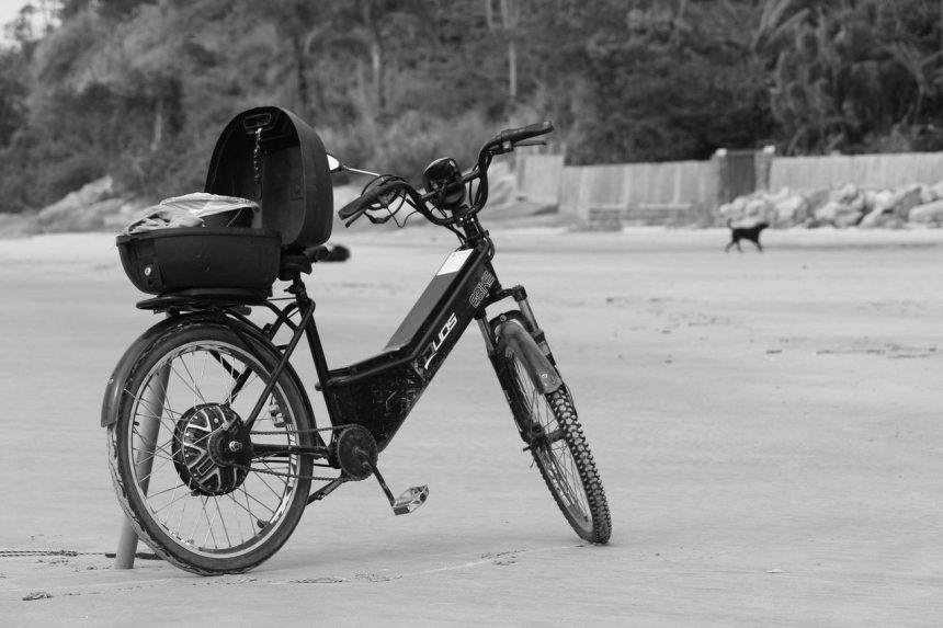 Bicicleta elétrica apoiada na areia da praia de Guaratuba, no Paraná, em imagem em preto e branco.