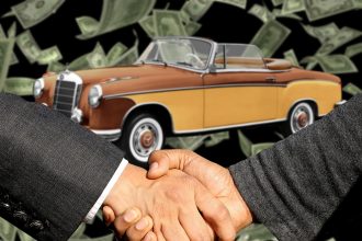 Comprador e vendedor apertam as mãos ao lado de um carro durante uma negociação de venda.