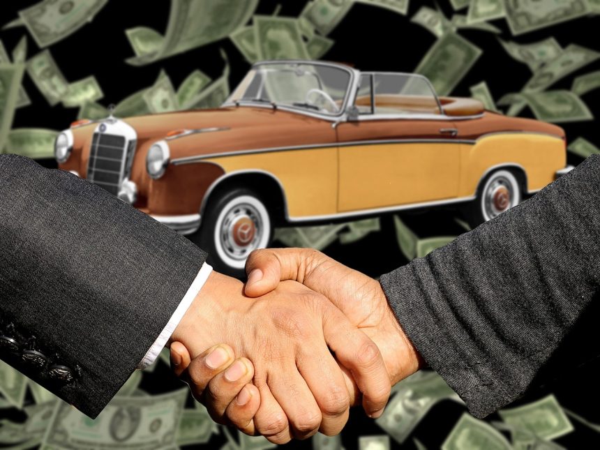 Comprador e vendedor apertam as mãos ao lado de um carro durante uma negociação de venda.
